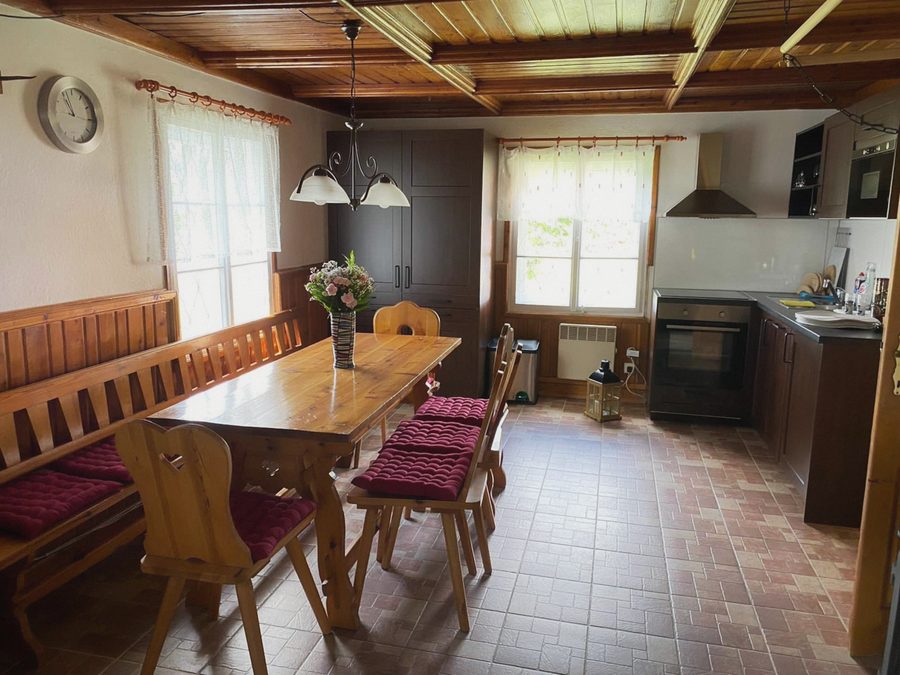Společenská místnost s dlouhým dřevěným stolem, lavicí a kuchyní