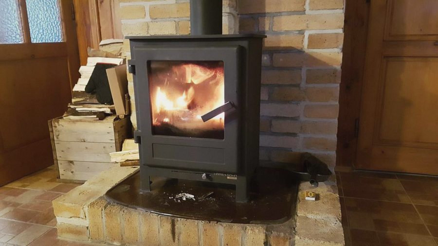 Hořící krbová kamna na cihlovém podstavci, vedle dřevo